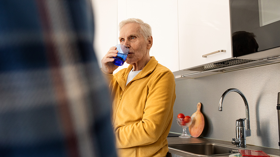 An older man is standing at the kitchen counter and drinking from a mug.