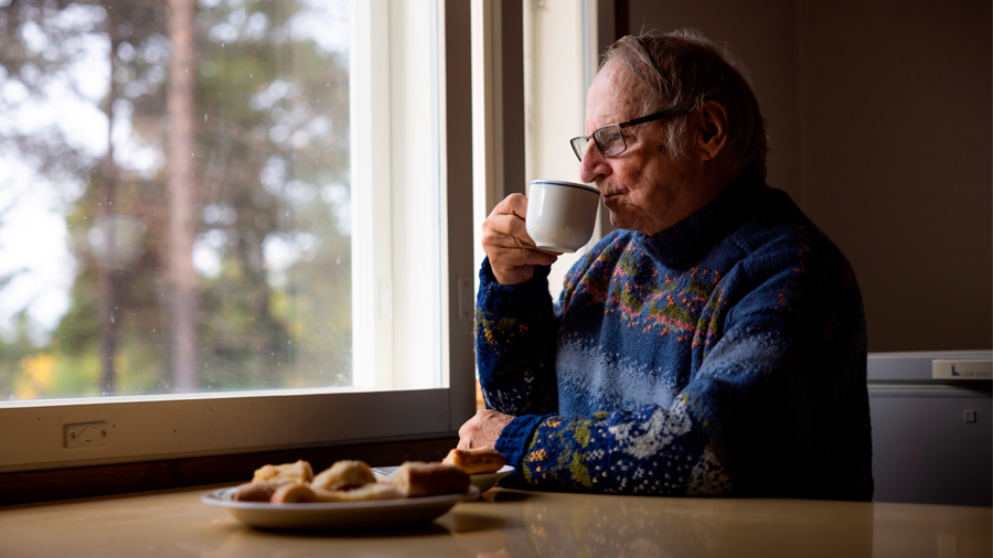 En senior dricker kaffe vid bordet och tittar ut genom fönstret