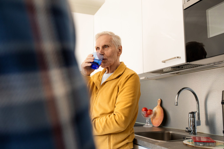 En pensionär dricker vatten i köket.
